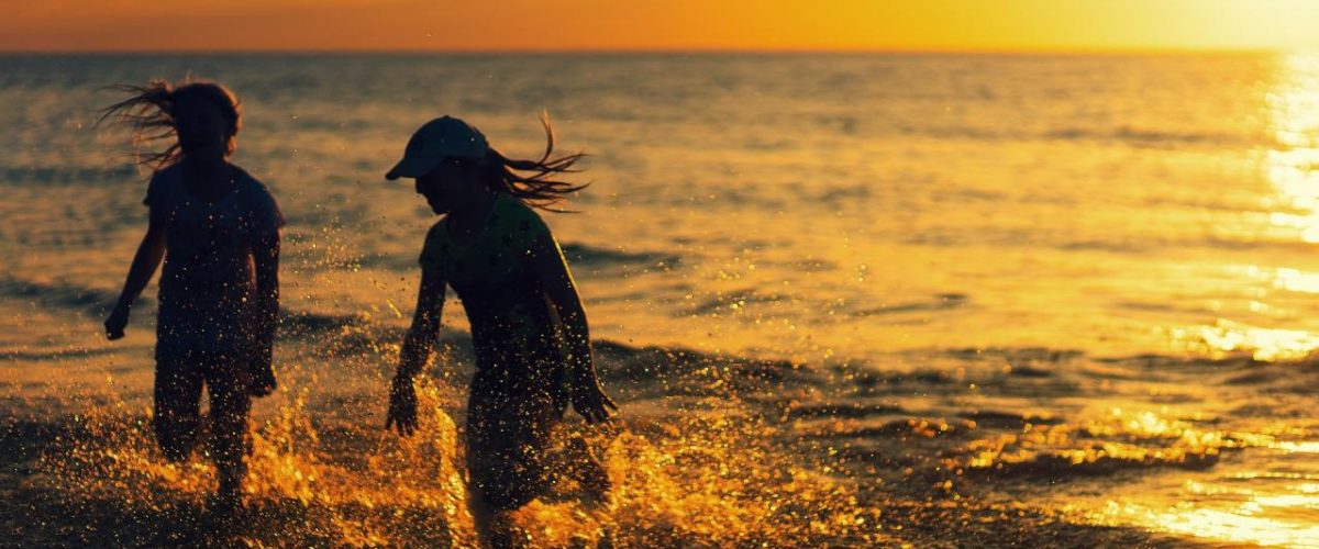 Mädchen spielen bei Sonnenuntergang am Strand